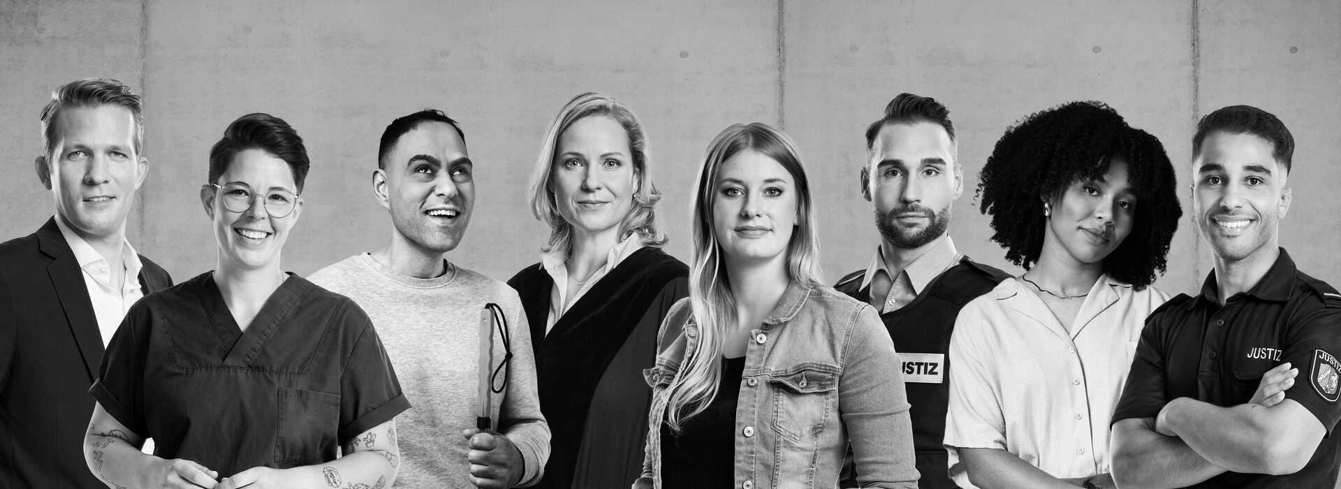 Auf dem schwarz-weiß Bild sind vier Frauen und vier Männer abgebildet. Manche Personen tragen Alltagskleidung und manche tragen Dienstkleidung. Ein Mann hält einen Langstock in der Hand.