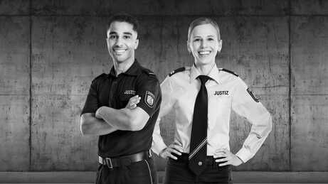 Auf dem schwarz-weiß Bild sind eine Frau und ein Mann in Dienstkleidung des Justizvollzugs zu sehen.